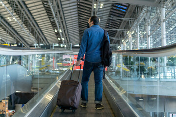 Young middle man travel by airplane with suitcase at airport terminal to flight gate. Asian guy with bagpack walking on travelator at airport. Traveler with luggage on moving walkway.Travel concept.