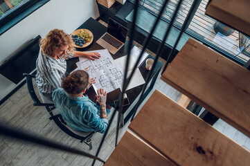 Happy couple using laptop and looking into blueprints of their new home