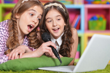 Portrait of two cute little girls singing karaoke with laptop