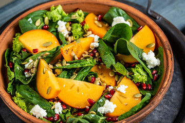 Gourmet salad with persimmon, avocado, pumpkin seeds, walnuts, pomegranate and arugula on a light...