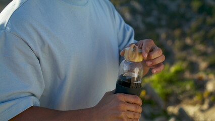 Athlete man drinking bottle water at ocean cliff closeup. Fit guy opening jug