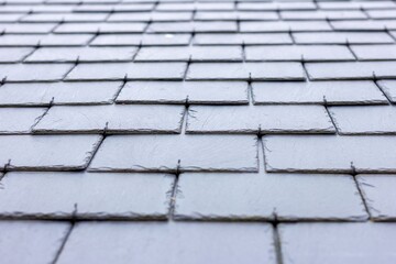 A close up portrait of a black, blue slate tile roof. The long lasting natural shingles are placed in a layered pattern and you can see the hooks keeping them in place.