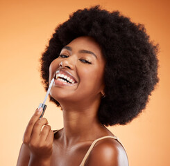 Obraz premium Lipgloss, smile and black woman excited about makeup against an orange studio background. Face portrait of a young African girl model with lipstick and cosmetic beauty product for care of lips
