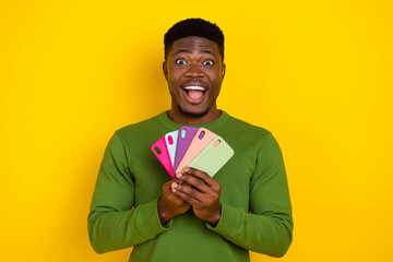 Portrait of handsome trendy cheerful crazy guy holidng in hands cell cases isolated on bright yellow color background