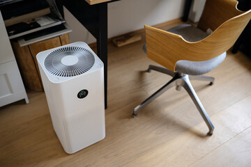 air purifier in the interior next to the workplace and armchair, cleaning from fine dust in the...