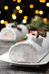 Fototapeta premium White chocolate yule log cake with christmas lights on wooden table