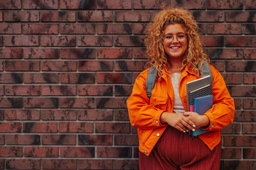 Caucasian female redhead student in front of brick wall with copy space.