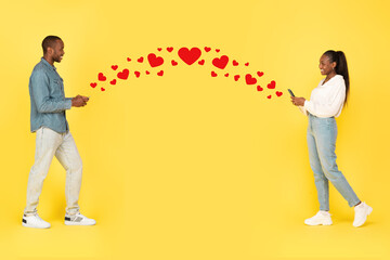 Fototapeta na wymiar African Couple Texting On Smartphones Sending Hearts Icons, Yellow Background
