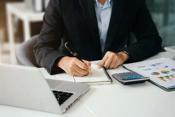 Businessman sitting at a table at home working on a laptop and writing down ideas in a notebook.