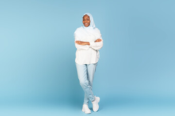 Happy african american woman in light hijab posing on blue studio background, full length shot,...