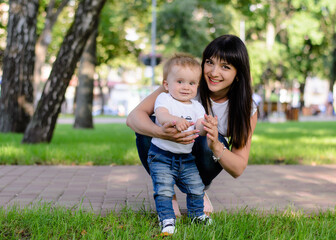 Happy mother with baby son in summer park. Happy motherhood. Mom teaches son to take the first steps