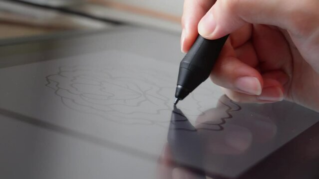 Woman's hand holding a pen stylus making an illustration using a digital drawing artist tablet. Close up macro shot.