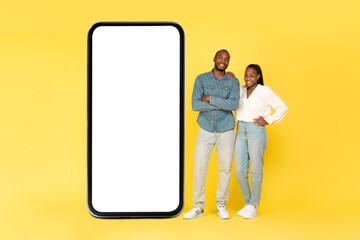 Happy Black Couple Standing Near Large Mobile Phone, Yellow Background