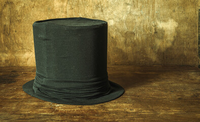 A large black top hat on a vintage wooden background. An old man's headdress. A magician's hat.