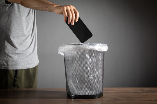 Male hand throws smartphone into the trash.