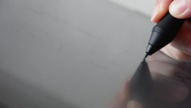 Woman's hand holding a pen stylus scrolling using a digital drawing artist tablet. Close up macro shot with copy space.