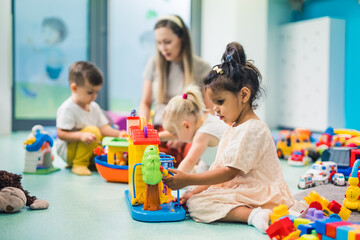 preschoolers building with toys and cubes and enjoying in kindergarten with teacher, creative activities for kids. High quality photo - obrazy, fototapety, plakaty
