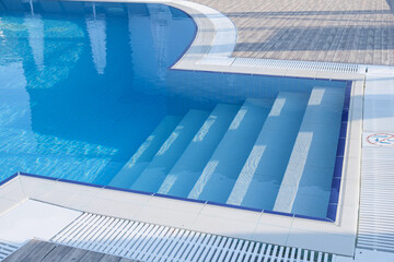 fiberglass plastic swimming pool entrance step with clean blue water at resort hotel spa area....