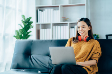 Beautiful young asian woman with headphones relaxing on the sofa. She is listening to music using smartphone . Chill out and leisure concept