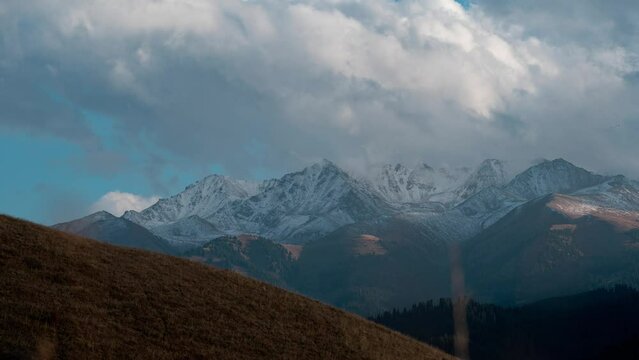 Beautiful time lapse of clouds drifting over rocky mountain peaks covered by snow. Scenic nature of Kyrgyzstan at Issyk-kul region