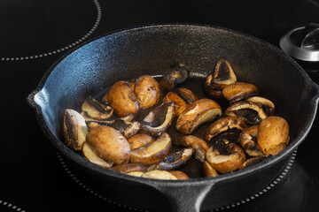 Frying chestnut mushrooms in a cast iron frying pan, on an electric hob stove