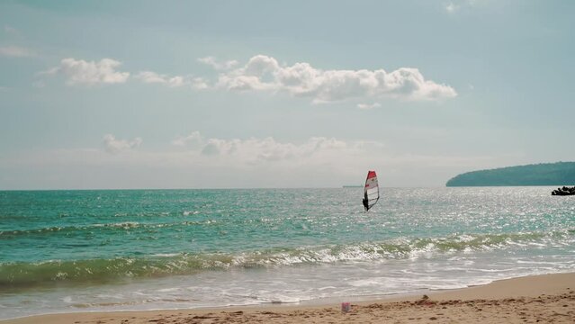 Windsurfer managing a sail of a windsurf board while floating near sea coast