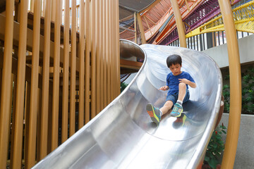 happy asian boy on playground. Kid slide down on slider at preschool school or kindergarten yard.