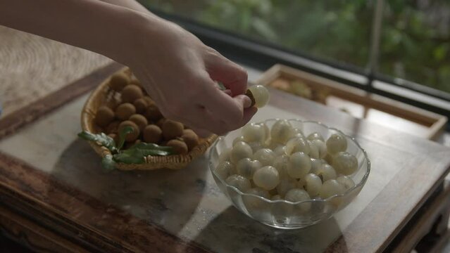 Person peeling longan fruit (Kelengkeng) and putting it in bowl on table