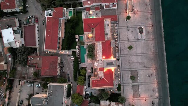 Flying away rotation bird view over the Poseidonion Grand Hotel and main squar in Spetses during sunset twilight while lights are light up on in the evening
