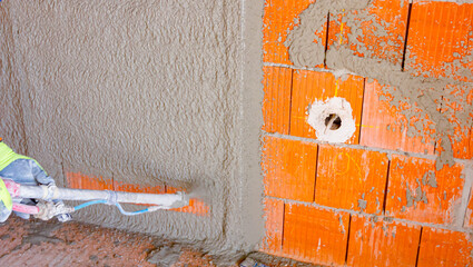 Craftsman holds mortar hose for plastering walls at indoor of unfinished residential edifice