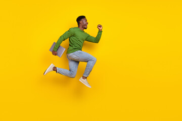 Full length body size view of handsome trendy guy jumping carrying laptop rejoicing isolated over vivid yellow color background