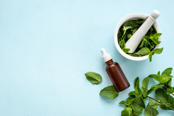 Bottle of essential peppermint oil with fresh green mint leaves