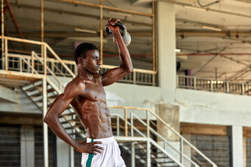 Athletic black young man lifting a heavy-weight in outdoor gym under the bridge. Healthy lifestyle concept