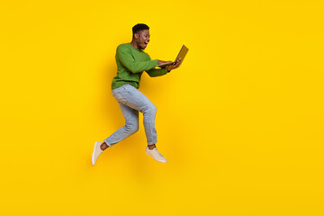 Fototapeta na wymiar Full length body size view of attractive cheery guy jumping using laptop web order buy isolated over vivid yellow color background