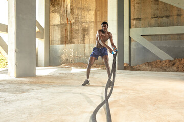 Rope workout. Sport man doing battle ropes exercise outdoor. Black male athlete exercising, doing functional fitness training with heavy rope