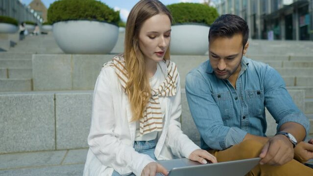 Smart Guy University Studen Helping Girlfriend to Solve Tasks in Online Test Using Laptop Outdoors Sitting at University Campus Area - slow motion medium shot