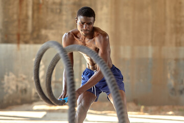 Obraz na płótnie Canvas Rope workout. Sport man doing battle ropes exercise outdoor. Black male athlete exercising, doing functional fitness training with heavy rope