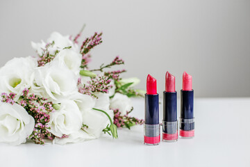 Obraz na płótnie Canvas Set of colored lipsticks. Concept of cosmetics and care. Beautiful flowers. Copy space