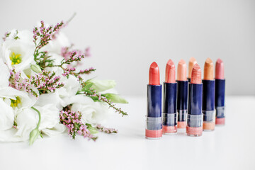 Obraz na płótnie Canvas Set of colored lipsticks. Concept of cosmetics and care. Beautiful flowers. Copy space