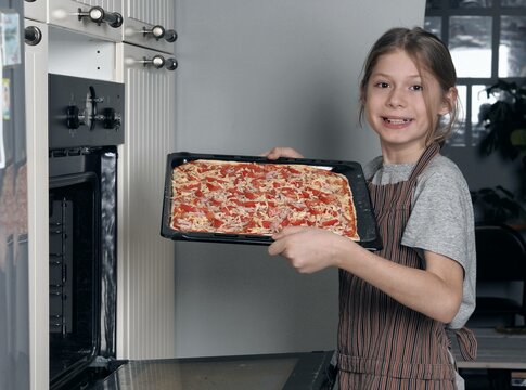 Food theme. The good mood of a teenager who put pizza in the kitchen oven. Activities, pastimes and hobbies of children. Homemade healthy food.