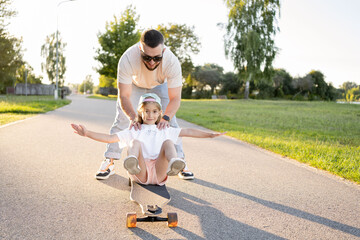 child girl sitting down on a skateboard and having his father push her.