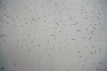 Glasscheibe mit Regentropfenmuster vor grauem diesigem Himmel bei Regen am Morgen im Herbst