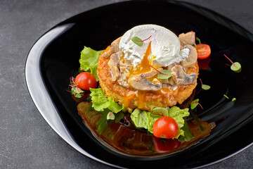 Beefsteak with mushrooms, poached egg and tomatoes on a black plate, black background
