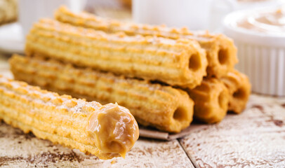 Churros, typical sweet from Brazil and America, fried and stuffed with sweet milk, covered in...