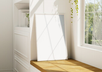 A blank white frame for a mockup It is placed next to a window where sunlight casts shadows. with clipping path.