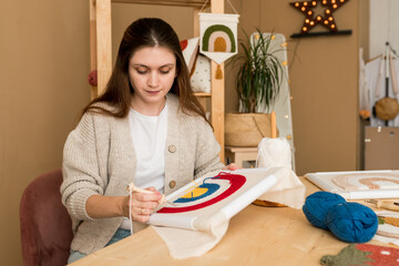 Young woman embroidering handmade picture rainbow on canvas in workshop. Modern punch needle kit...