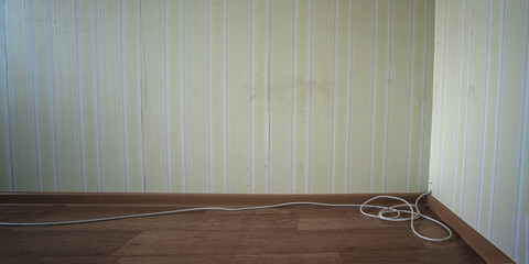 TV cable is stretched along wall and lies near wooden plinth on floor