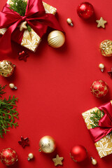 Christmas vertical banner. Frame made of gift boxes with red ribbon bow, baubles, Xmas decorations, fir branches on red background. Flat lay, top view, copy space.