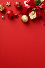 Christmas vertical banner. Frame made of gift boxes with red ribbon bow, baubles, decorations on red background. Flat lay, top view, copy space.