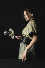 portrait of a beautiful woman with exotic flowers in a kimono on a black background with lighting from the back	